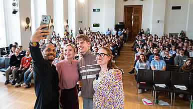 Vier Menschen machen auf einer Bühne ein Selfie mit dem Publikum im Hintergrund