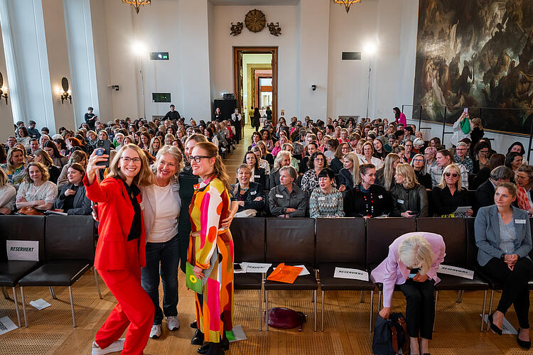 Vier Frauen posieren vor sitzendem Publikum für ein Selfie