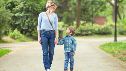Eine Frau und ein kleiner Junge gehen Hand in Hand einen Weg entlang und blicken sich in die Augen.