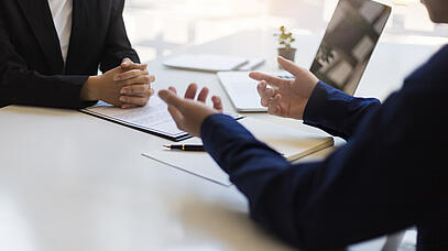 2 Personen sitzen im Anzug am Tisch und besprechen sich