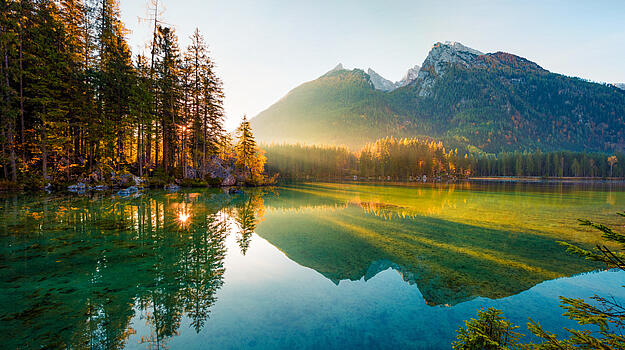 Blick auf Berge, See und Bäume mit oranger Sonneneinstrahlung