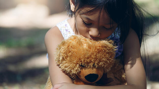Ein Mädchen umarmt traurig seinen Teddybären.