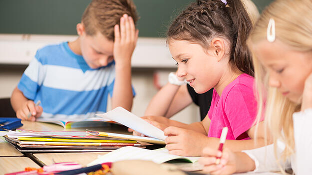Drei Grundschulkinder, die in der Schule sitzen und lernen.