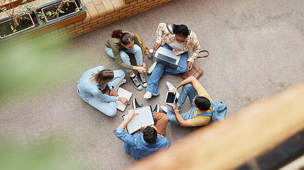 Fünf Studierende sitzen im Kreis, zum Teil mit Laptop und unterhalten sich. Von oben fotografiert.