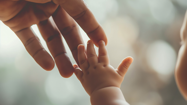 Eine Baby greift mit seiner kleinen Hand nach dem Finger einer erwachsenen Hand