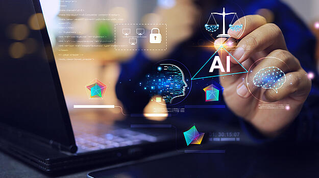 Eine digitale Zeichnung mit der Aufschrift AI wird von einer Hand mit Laserpointer angetippt. Daneben steht ein Laptop.