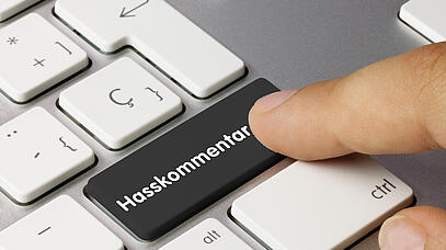 Finger drückt auf Computer-Tastatur eine schwarze Taste mit der Aufschrift "Hasskommentar".