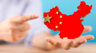 Eine unscharfe Hand im Hintergrund deutet auf den im Vordergrund stehenden Umriss von China, der mit der chinesischen Flagge ausgefüllt ist.