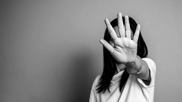 Eine Frau streckt abwehrend ihre Hand nach vorne, so dass sie ihr Gesicht verdeckt.