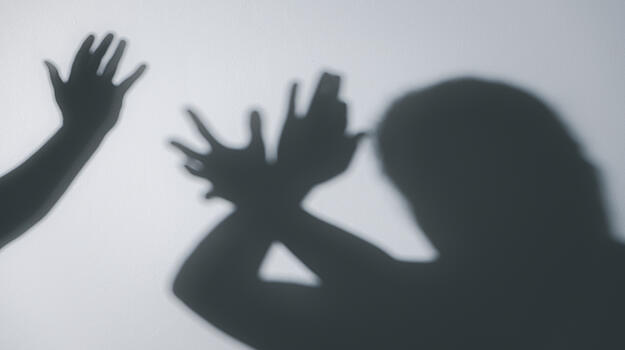 Das Bild zeigt den Schatten eines Menschen, der seine Arme zu einer Abwehrhaltung reckt. Daneben ist der Schatten einer erhobenen Hand zu sehen.
