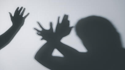 Das Bild zeigt den Schatten eines Menschen, der seine Arme zu einer Abwehrhaltung reckt. Daneben ist der Schatten einer erhobenen Hand zu sehen.
