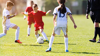 Kinder in roten und weißen Trikots mit einem Fußball