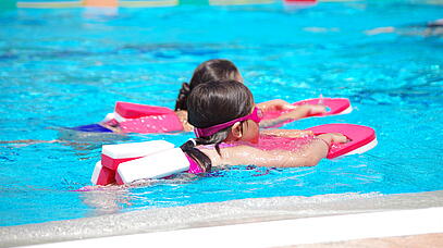 Zwei Kinder, die mit Schwimmhilfen im Schwimmbecken schwimmen lernen.