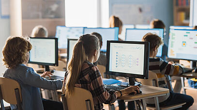 Kinder sitzen in einem Klassenzimmer vor einem Computer-Bildschirm.