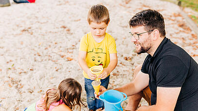 Abgeordnerter Johannes Becher sitzt mit 2 Kindern im Sandkasten.