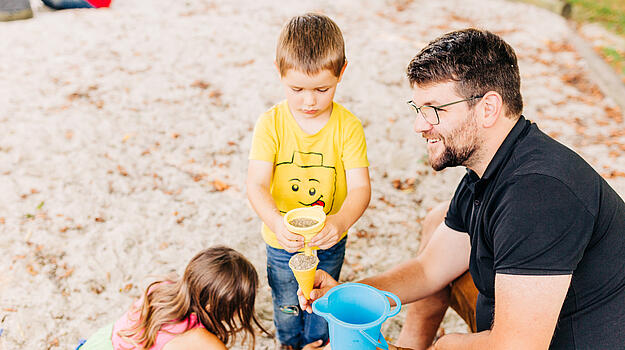 Abgeordnerter Johannes Becher sitzt mit 2 Kindern im Sandkasten.