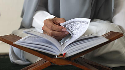 Eine Person blättert in einem Buch mit arabischen Schriftzeichen, das auf einem Halter liegt.