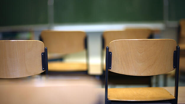 Leere Stühle in Klassenzimmer oder Hörsaal. Vorne steht eine grüne Tafel.