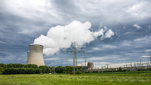 Auf der linken Bildseite stehen große Kühltürme. Auf der rechten Seite befinden sich Stromleitungen und Umspannwerke. Der Himmel ist von dunklen Wolken bedeckt.  