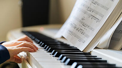 Kleine Hände liegen auf einer Klavier-Tastatur. Davor stehen Musiknoten.