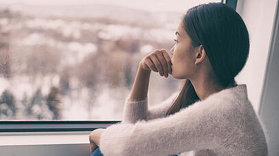 Eine Frau sitzt am Fenster und schaut hinaus.