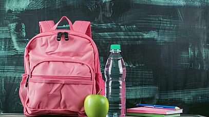 Pinker Rucksack, danaben ein Apfel und eine Wasserflasche