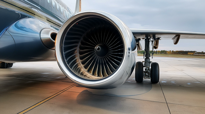Eine große Turbine hängt am Flügel eines Flugzeugs, das auf einem Betonboden steht. Daneben ist das Fahrwerk zu sehen.