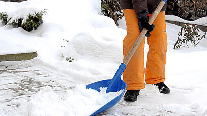 Person mit orangener Schneehose beim Schneeschaufeln