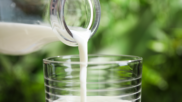 Hände, die Milch von einer Flasche in ein Glas einschenken