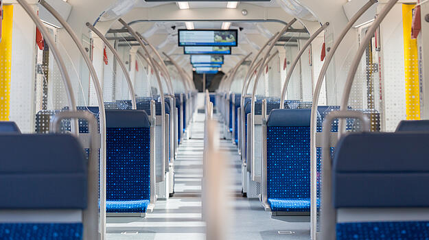 Im inneren einer S-Bahn sind auf beiden Seiten Sitze zu sehen. Über dem Mittelgang hängen Bildschirme