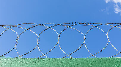 Stacheldrahtrollen auf einer Mauer vor blauem Himmel.