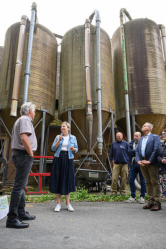 Katharina Schulze spricht in ein Mikrofon, im Hintergrund drei große Silos.