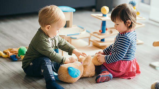 Zwei kleine Kinder spielen zusammen mit einem Kuscheltier. 