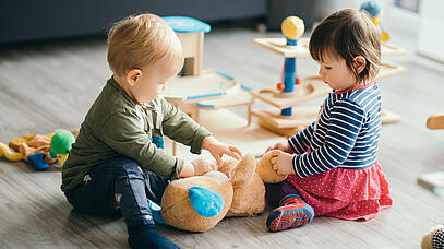 Zwei kleine Kinder spielen zusammen mit einem Kuscheltier. 