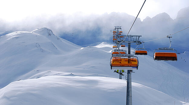 Ein Sessellift hängt von Pfosten zu Pfosten über eine Skipiste. Weiter oben verliert er sich im Nebel. 