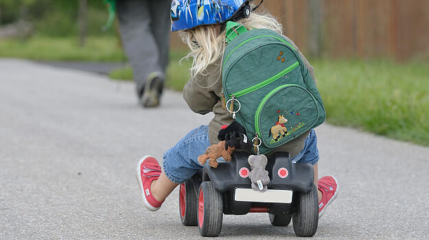 Kind mit Rucksack fährt Bobbycar.
