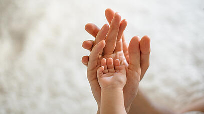 Babyhand liegt in zwei erwachsenen Händen.